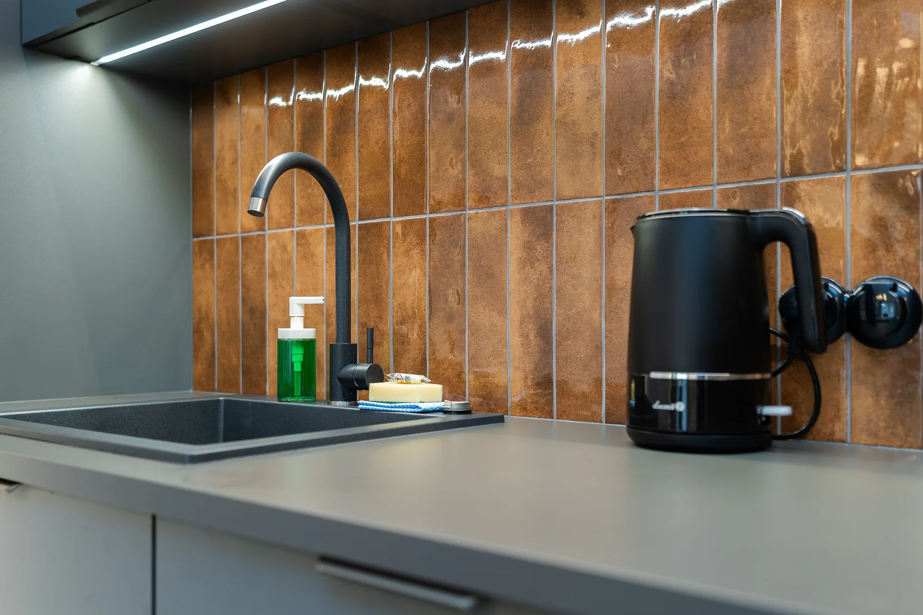Kitchen counter detail with a rust-coloured tiled splashback, sink and kettle