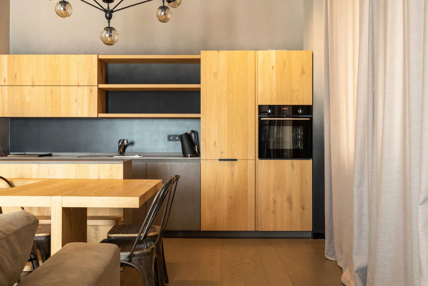 Run of tall oak cupboards beside a built-in oven, with the oak table in the foreground