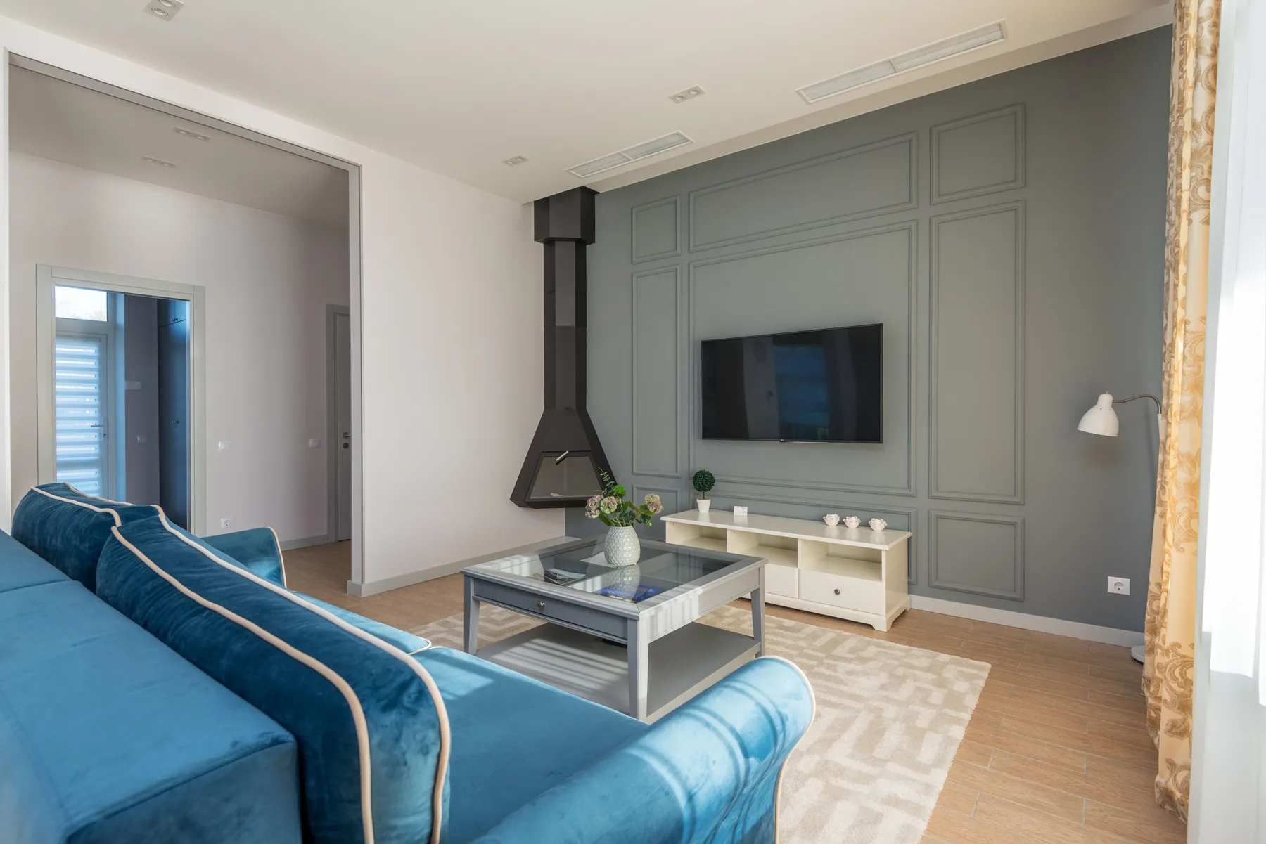 Drawing room with grey-green panelled wall, blue velvet sofa and a black wood-burning stove