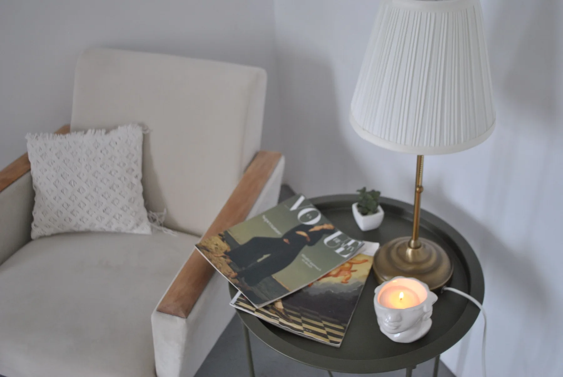 An armchair and side table in a finished room, with magazines and a lit candle