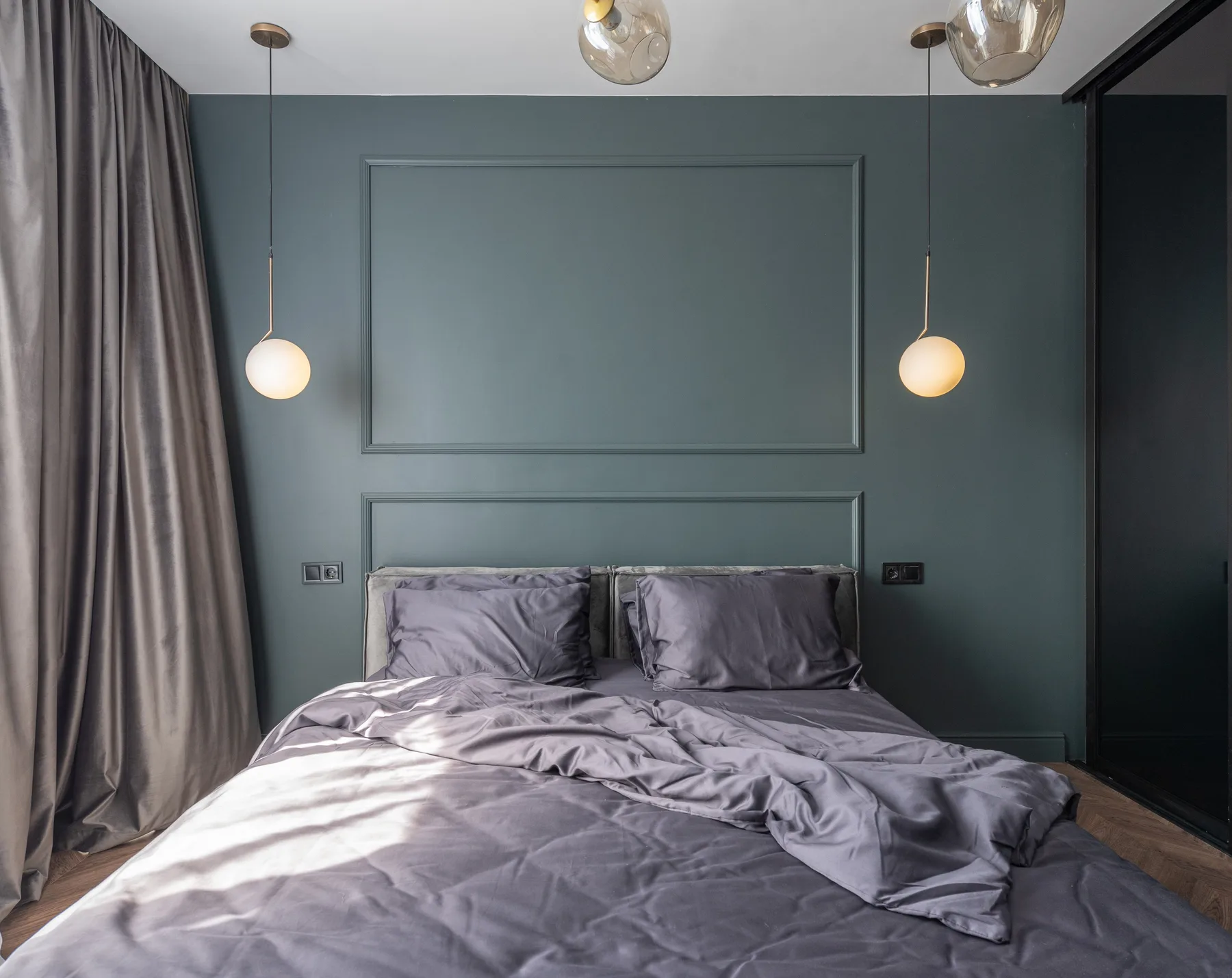 Bedroom with deep blue-green panelled walls, low opal globe pendants either side of the bed