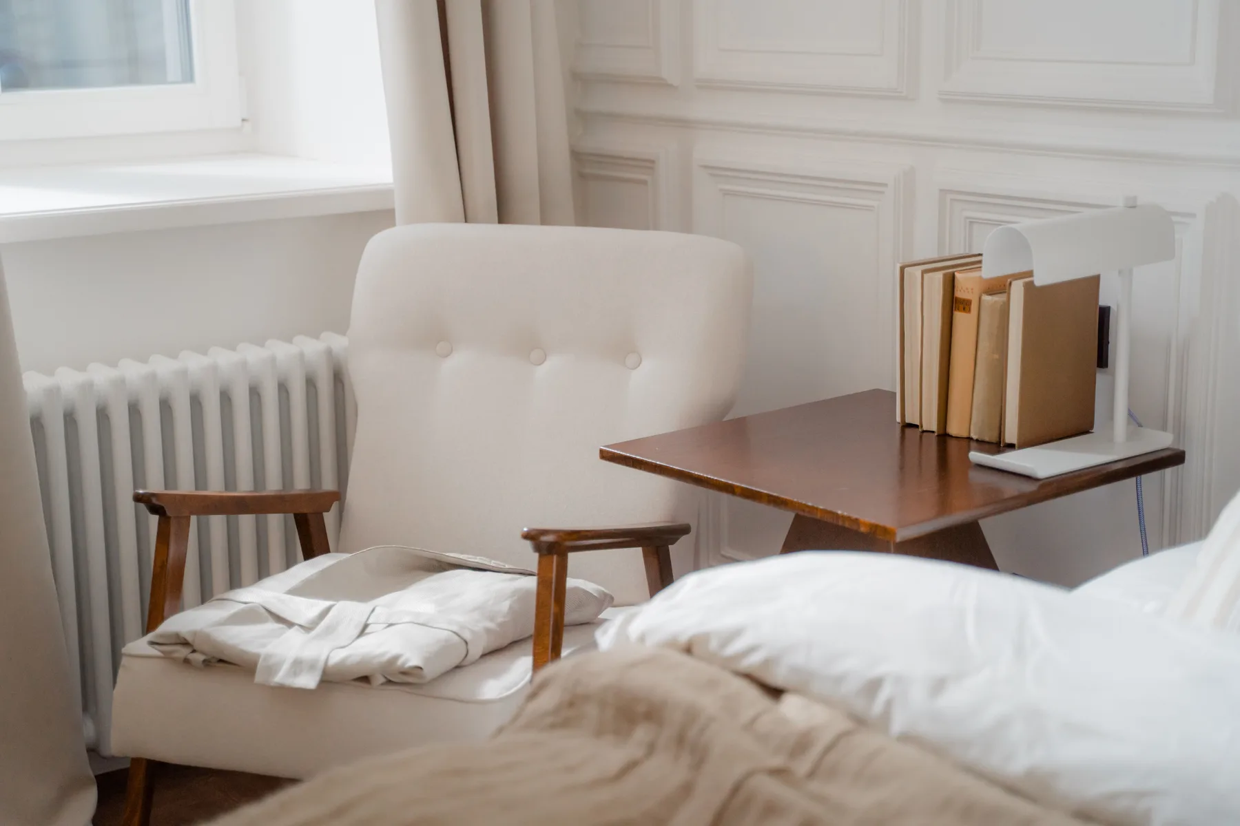 Corner of the bedroom with an upholstered chair, a small writing table and a folded robe