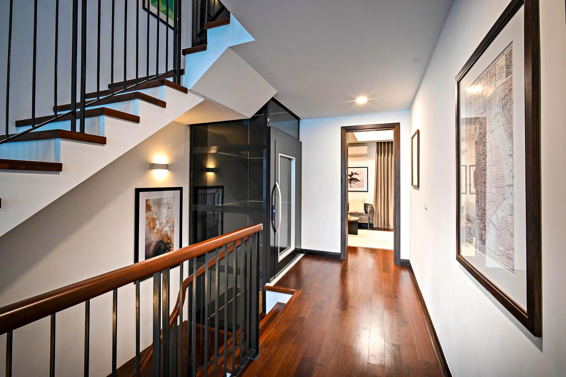Corridor with timber floor, framed pictures and a view through to the stair